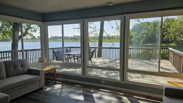 A sunroom with large windows overlooking a lake, a sofa, and a small table. - Charming Lakefront Retreat with Sandy Beach – Perfect Getaway  (Shelbyville)