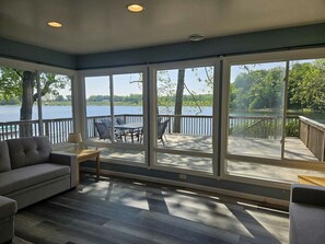 Un solarium con amplias ventanas con vistas a un lago, un sofá y una mesita.