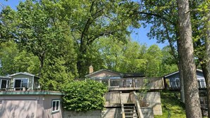 A residential property with a main house, a detached garage, and a covered outdoor area with a wooden deck and stairs. - Charming Lakefront Retreat with Sandy Beach – Perfect Getaway  (Shelbyville)