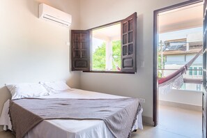 A bedroom with a bed, an open window, a hammock outside, and an air conditioning unit on the wall. - Cassa em Cond beira-mar-4qts-SH088B (Tamandaré)