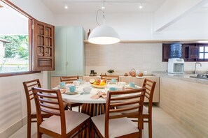 A modern kitchen with a round dining table, wooden chairs, and a hanging light fixture. - Cassa em Cond beira-mar-4qts-SH088B (Tamandaré)