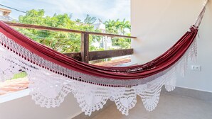 A hammock with white lace, a balcony, and a view of greenery.