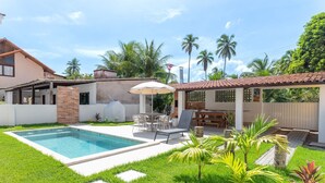 A backyard with a swimming pool, outdoor furniture, and a covered patio area.
