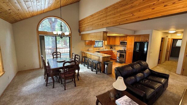 A spacious living area with a dining table, leather sofa, and a kitchen with wooden cabinets and appliances.