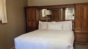 A bedroom with a large bed, wooden headboard, a mirror, and a nightstand.