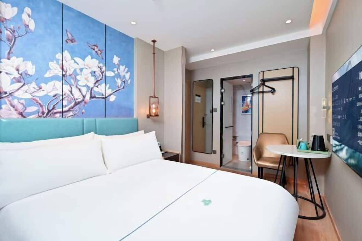 A hotel room with a large bed, a painting of flowers, a desk with a chair, and a mirror.