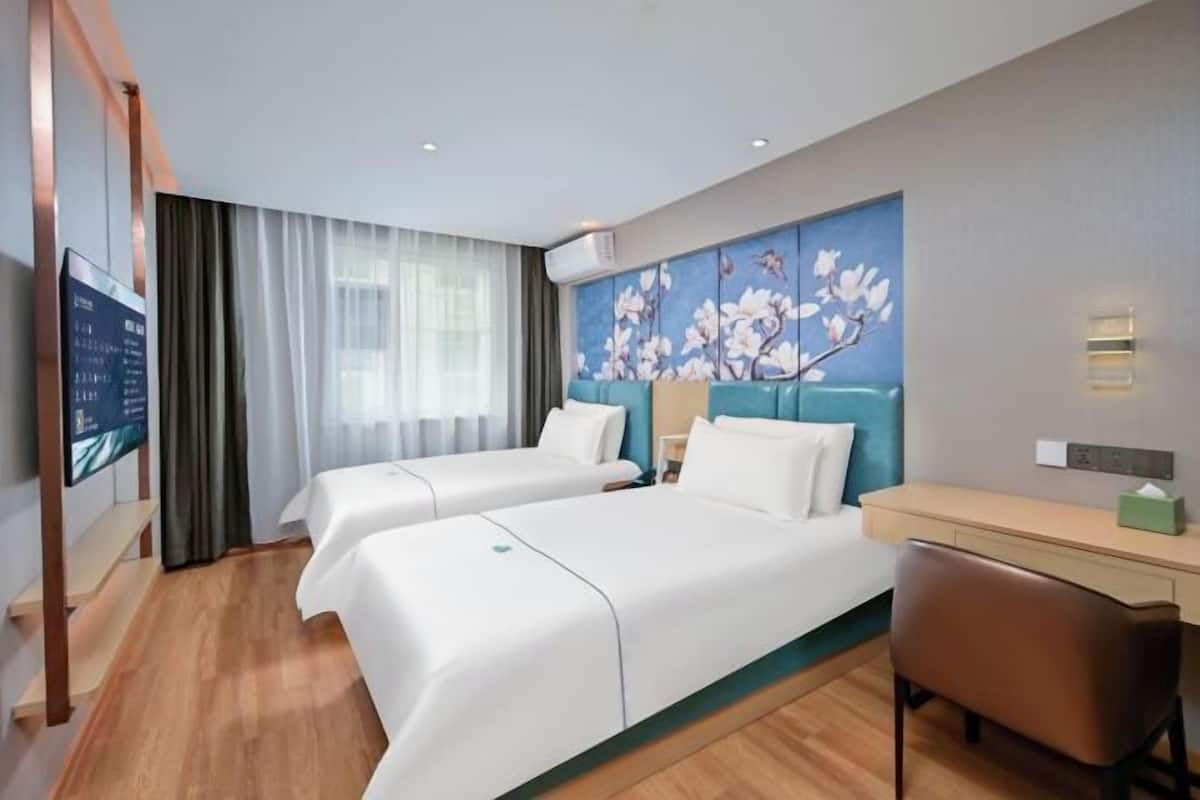 A hotel room with two beds, a desk, a chair, a TV, and a painting on the wall.