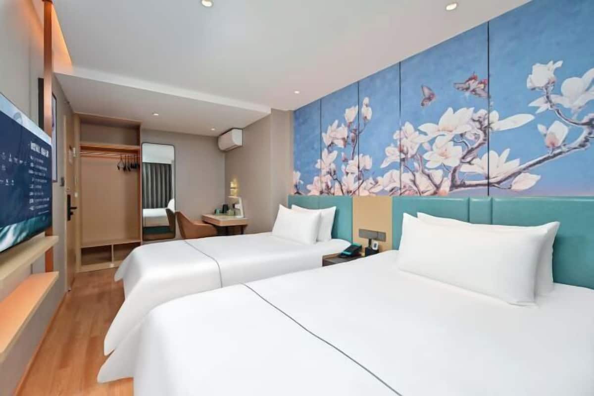 A hotel room with two beds, a large floral mural, a desk with a chair, and a television.