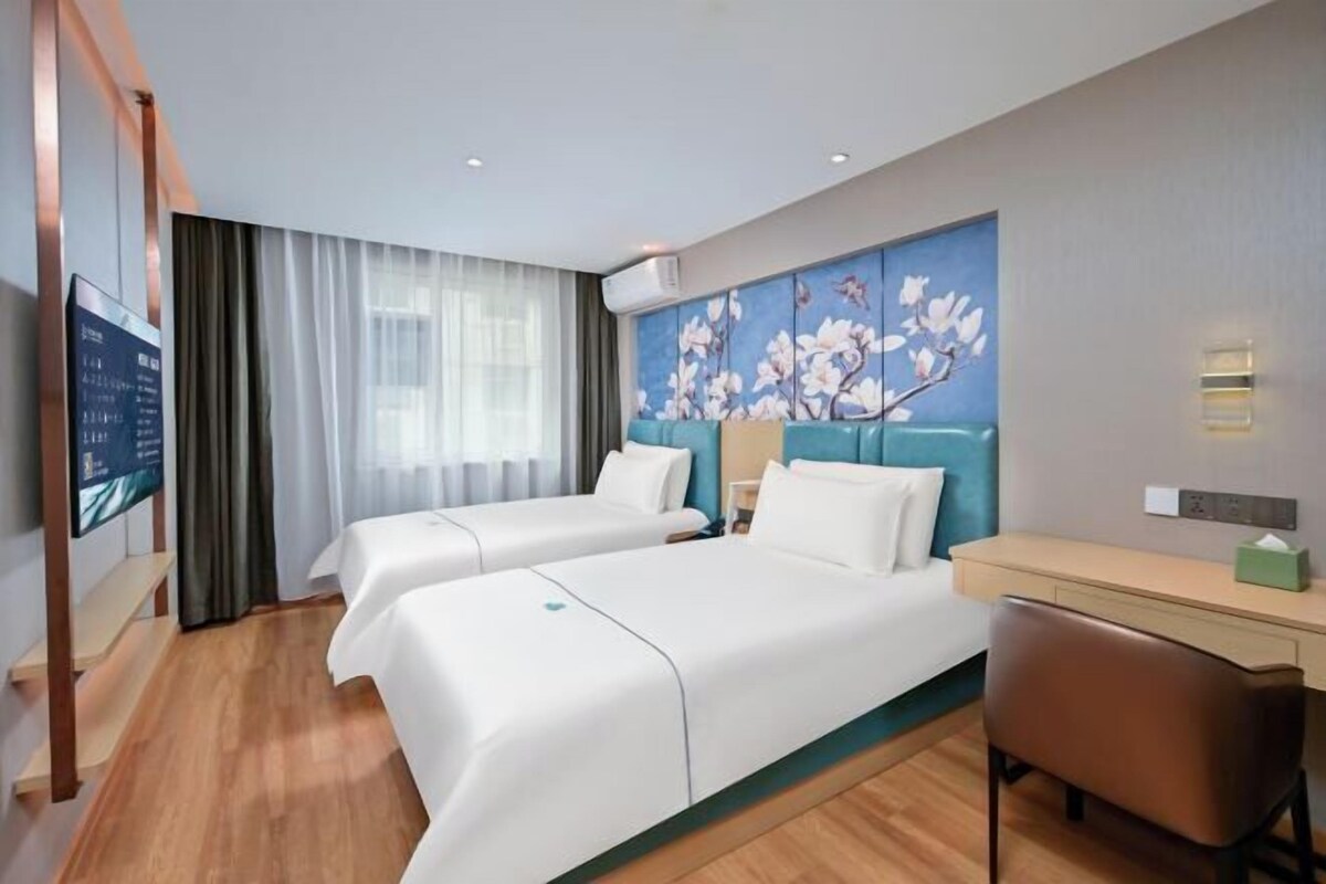 A hotel room with two beds, a desk, a chair, a TV, and a painting on the wall.