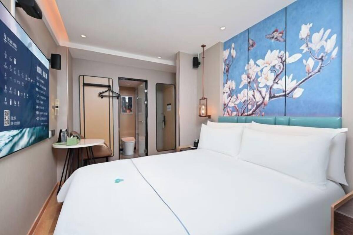 A hotel room with a large bed, a small table, a mirror, and a painting of flowers on the wall.