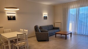 Un salon comprenant une table à manger, des chaises, un canapé, une table basse et deux lampes fixées au mur.