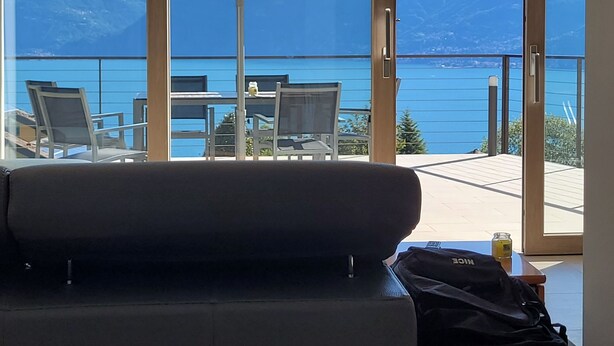 Une pièce comprenant un canapé, une table avec des chaises, un grand parapluie et une vue sur un lac et des montagnes.