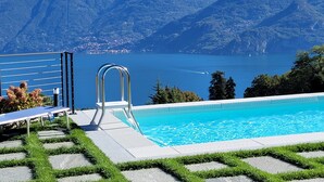 Une piscine dotée d’un escalier en métal, entourée de pelouse et de chemins en pierre, et offrant une vue sur un lac avec des montagnes en arrière-plan.