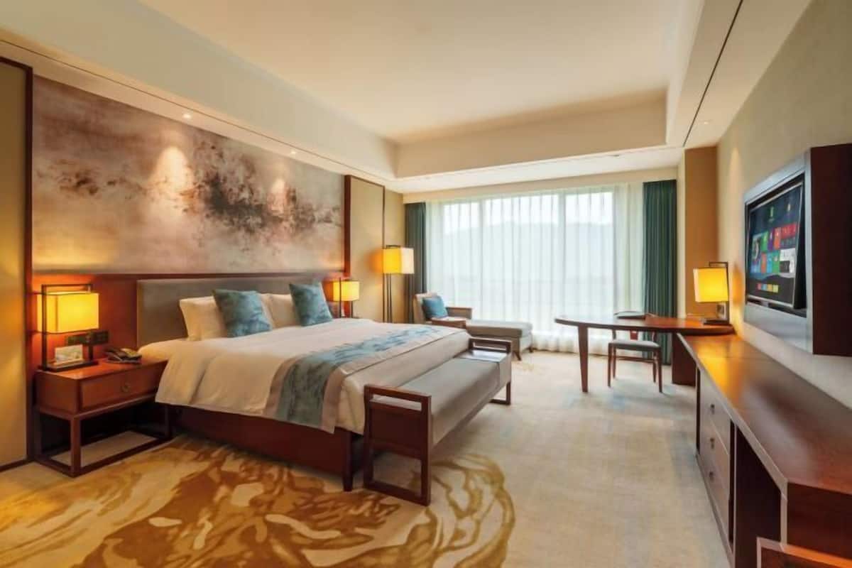 A hotel room with a large bed, a desk, a chair, a television, and a painting on the wall.