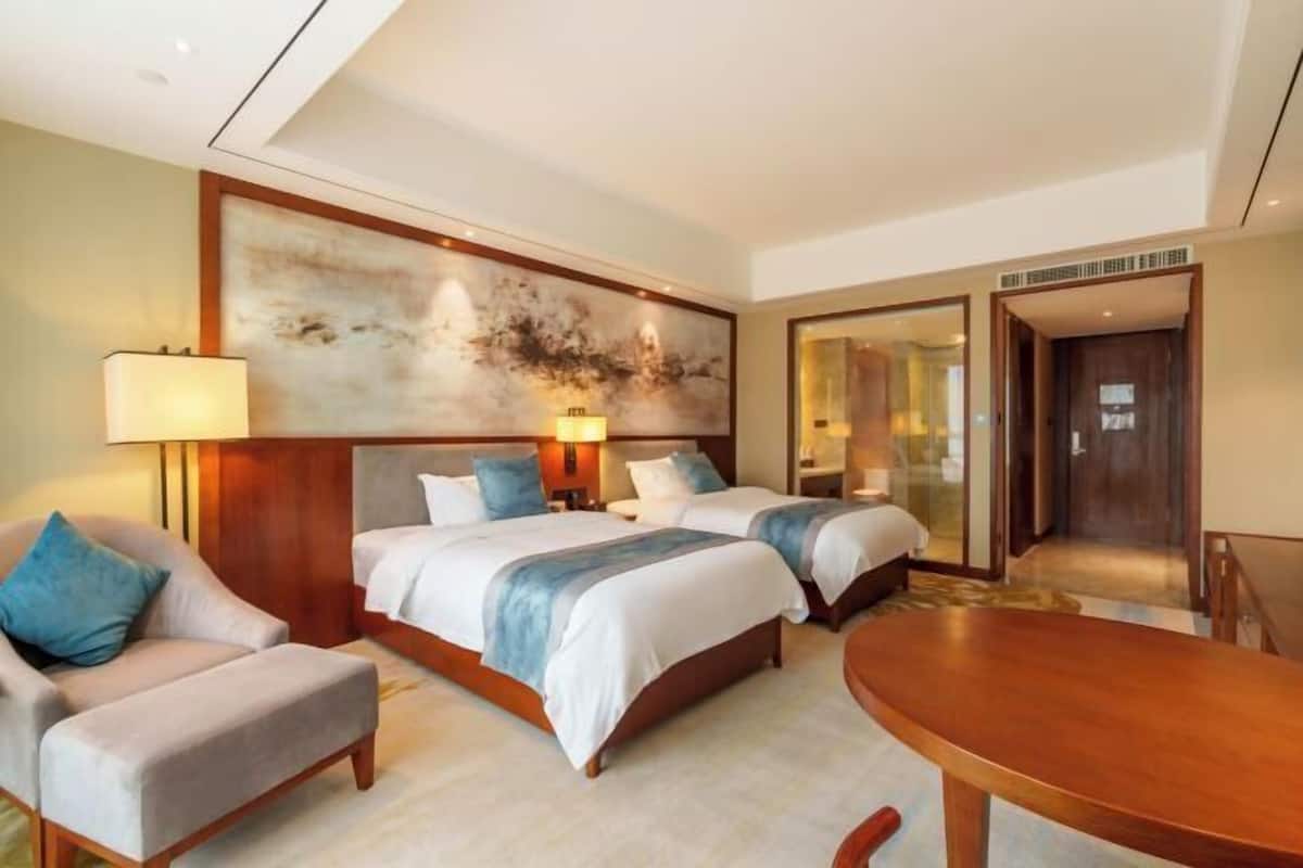A hotel room with two beds, a sitting area with a chair, a dining table, and a large abstract painting on the wall.