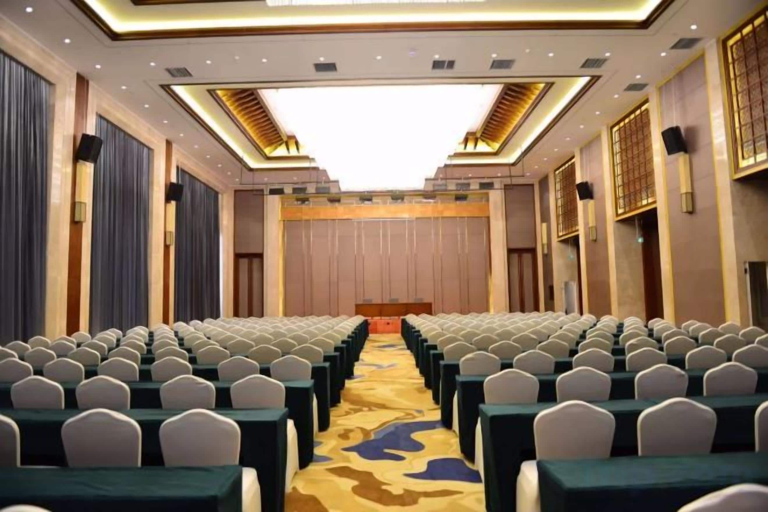 Un salón de conferencias con filas de sillas, un atril y piso alfombrado.