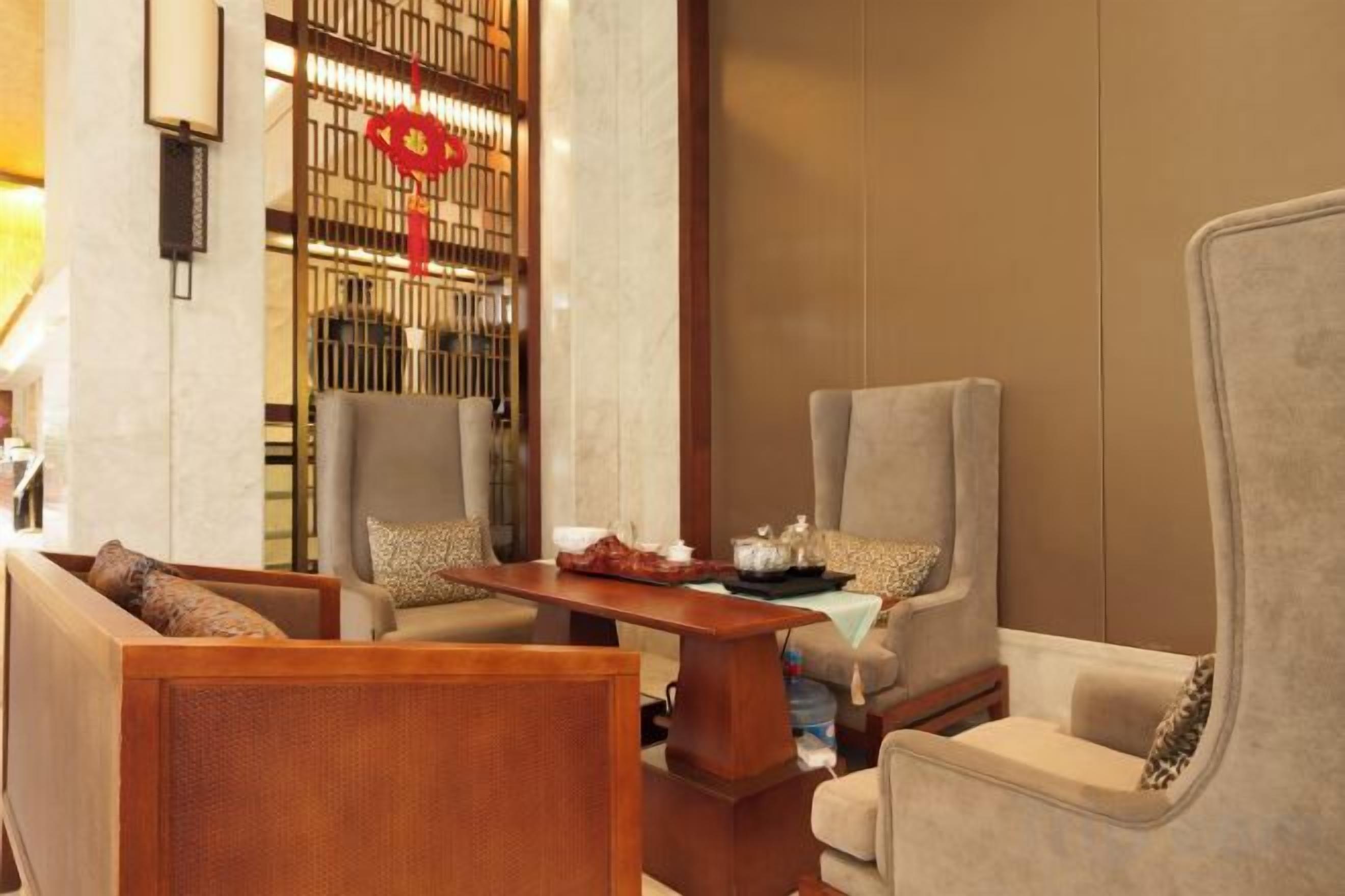 Un área de descanso con dos sillones y un sofá, una mesa de centro de madera, y una pared decorativa con un adorno rojo.