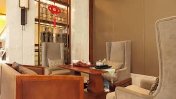 Un área de descanso con dos sillones y un sofá, una mesa de centro de madera, y una pared decorativa con un adorno rojo.