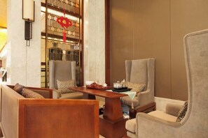 A seating area with two armchairs and a sofa, a wooden coffee table, and a decorative wall with a red ornament. - Kailong Holiday Hotel (Longling)