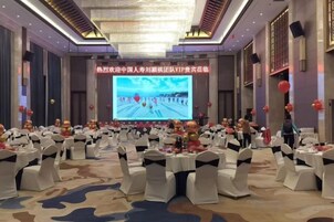 Un salón de banquetes con mesas redondas, sillas y una pantalla grande mostrando una presentación.
