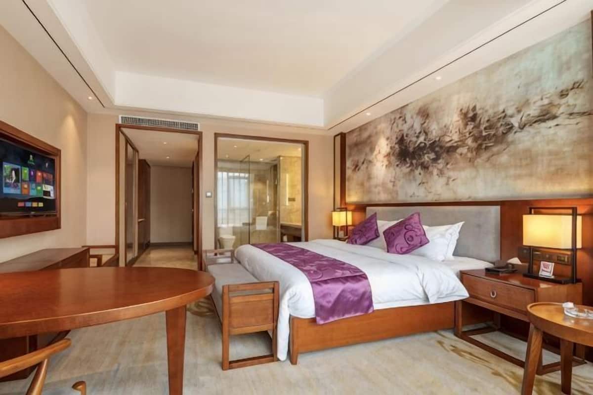 A hotel room with a bed, bedside table, lamp, TV, and a large abstract painting on the wall.