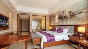 A hotel room with a bed, bedside table, lamp, TV, and a large abstract painting on the wall.