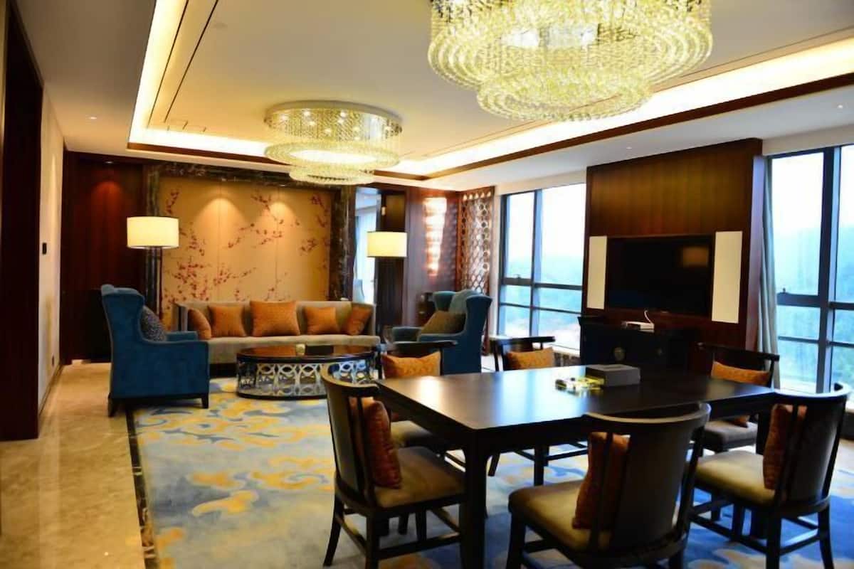 A modern hotel room with a dining area, large windows, and a chandelier.