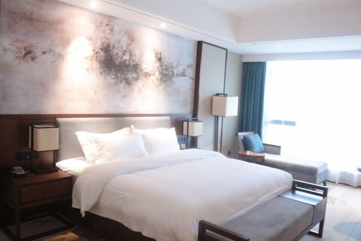 A hotel room with a large bed, bedside tables with lamps, a sofa, and a view of the outdoors.