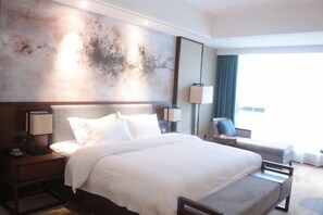 A hotel room with a large bed, bedside tables with lamps, a sofa, and a view of the outdoors.