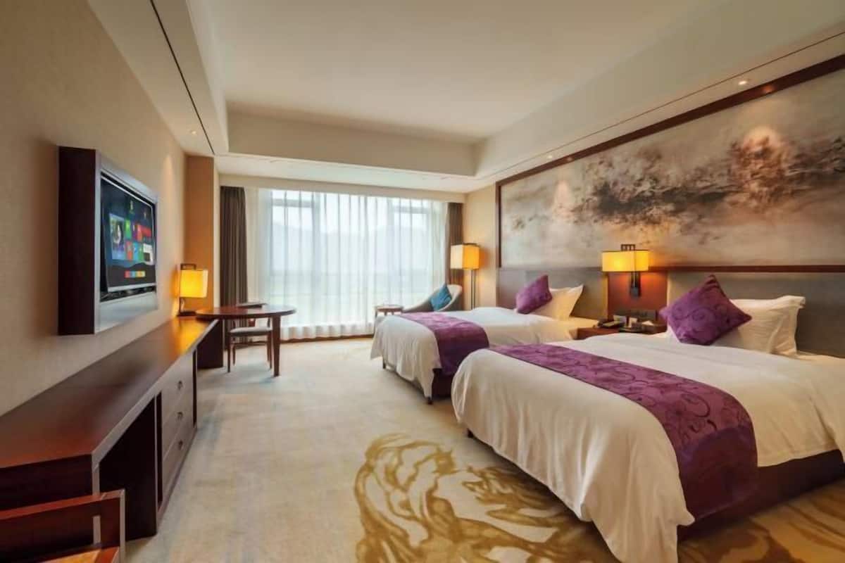 A hotel room with two beds, a TV, a desk, and a large painting on the wall.