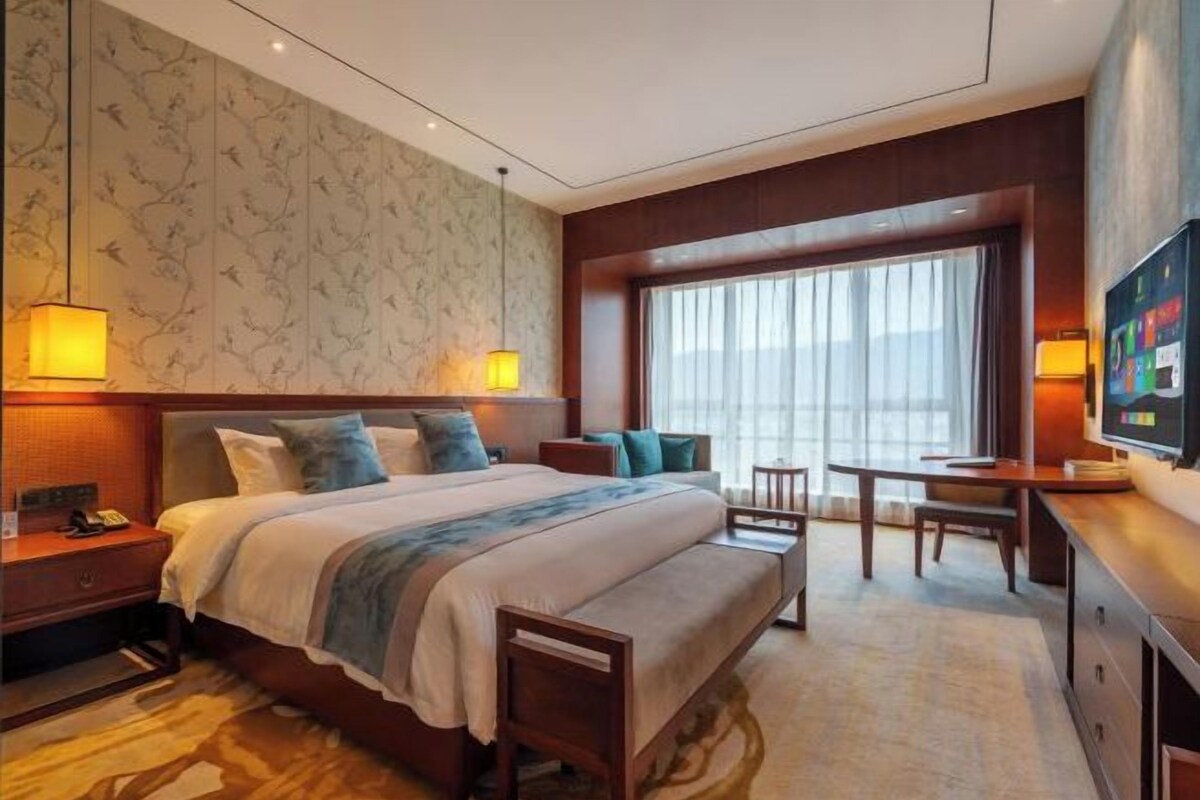 A hotel room with a large bed, bedside tables, a desk, and a TV.