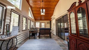 L’intérieur d’une cabane en rondins, avec un plafond en bois, de grandes fenêtres, un coin repas et une grande armoire en bois.