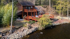 Une cabane dotée d’une terrasse, entourée d’arbres et bordée par un plan d’eau.