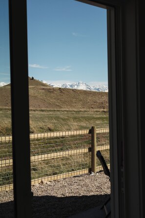 Blick durch ein Fenster auf eine gebirgige Landschaft mit einem Zaun und einem Holzbalken.