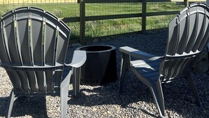 A patio with two Adirondack chairs, a table, and a grill, overlooking a grassy field and mountains. - Farm stay near Yellowstone, Livingston, Bozeman, hiking, fishing, skiing (Livingston)