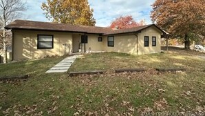 Une maison à deux étages avec un porche à l’avant, un garage et un petit jardin devant, avec un chemin menant à l’entrée.