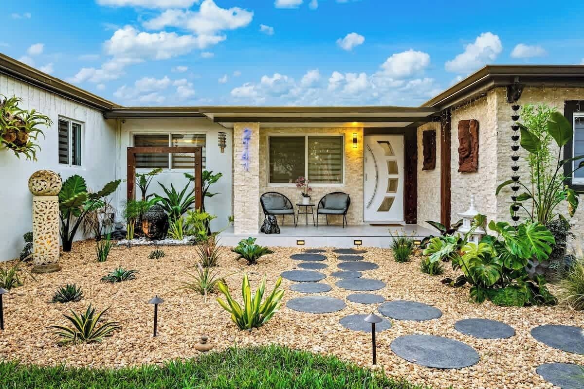 Una casa moderna con fachada de piedra, un patio con camino de piedra y mobiliario exterior.