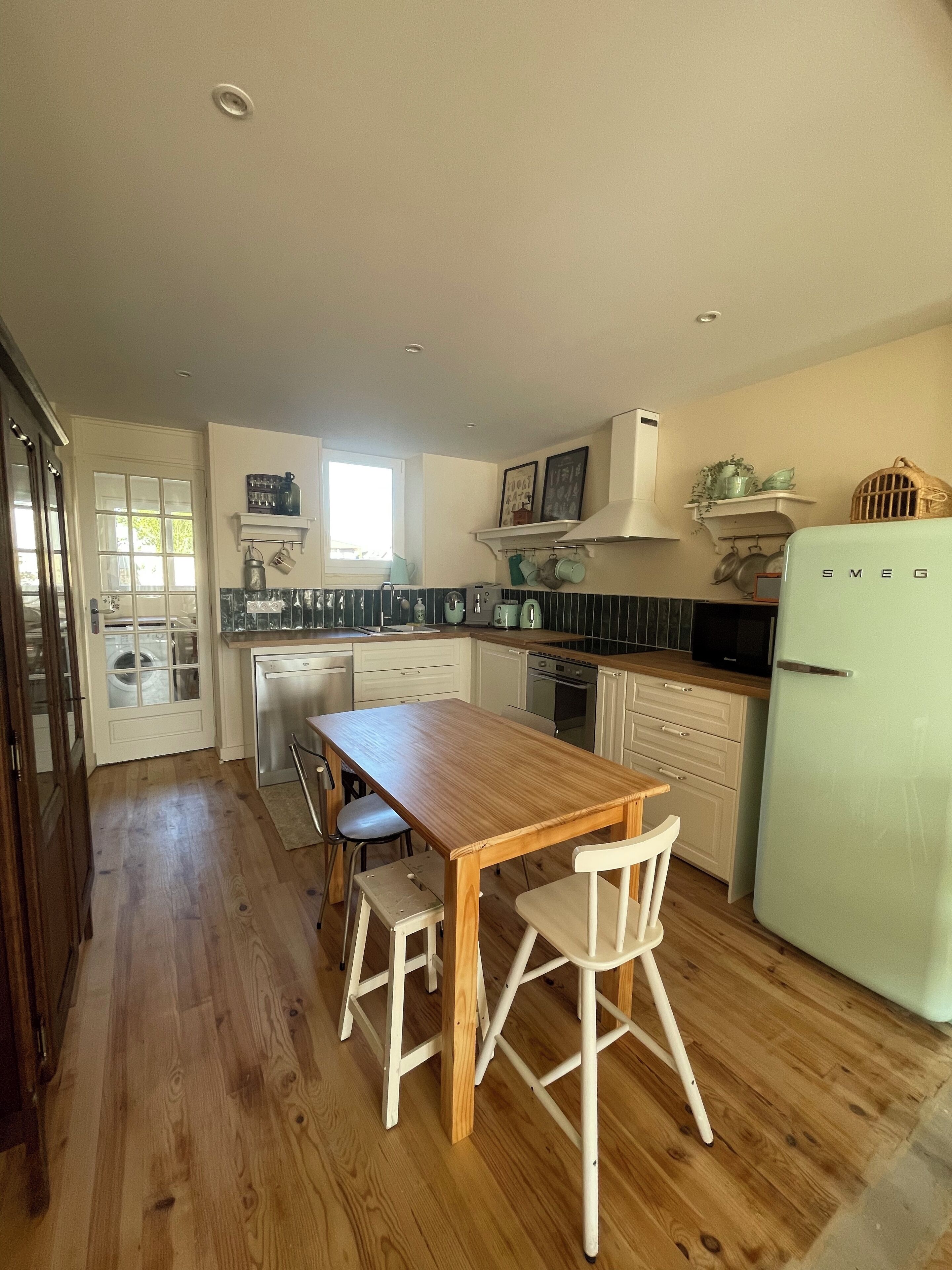 A kitchen with a wooden table and chairs, a refrigerator, and a window.
