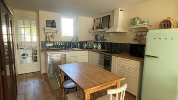 A kitchen with a wooden table and chairs, a refrigerator, and a window.