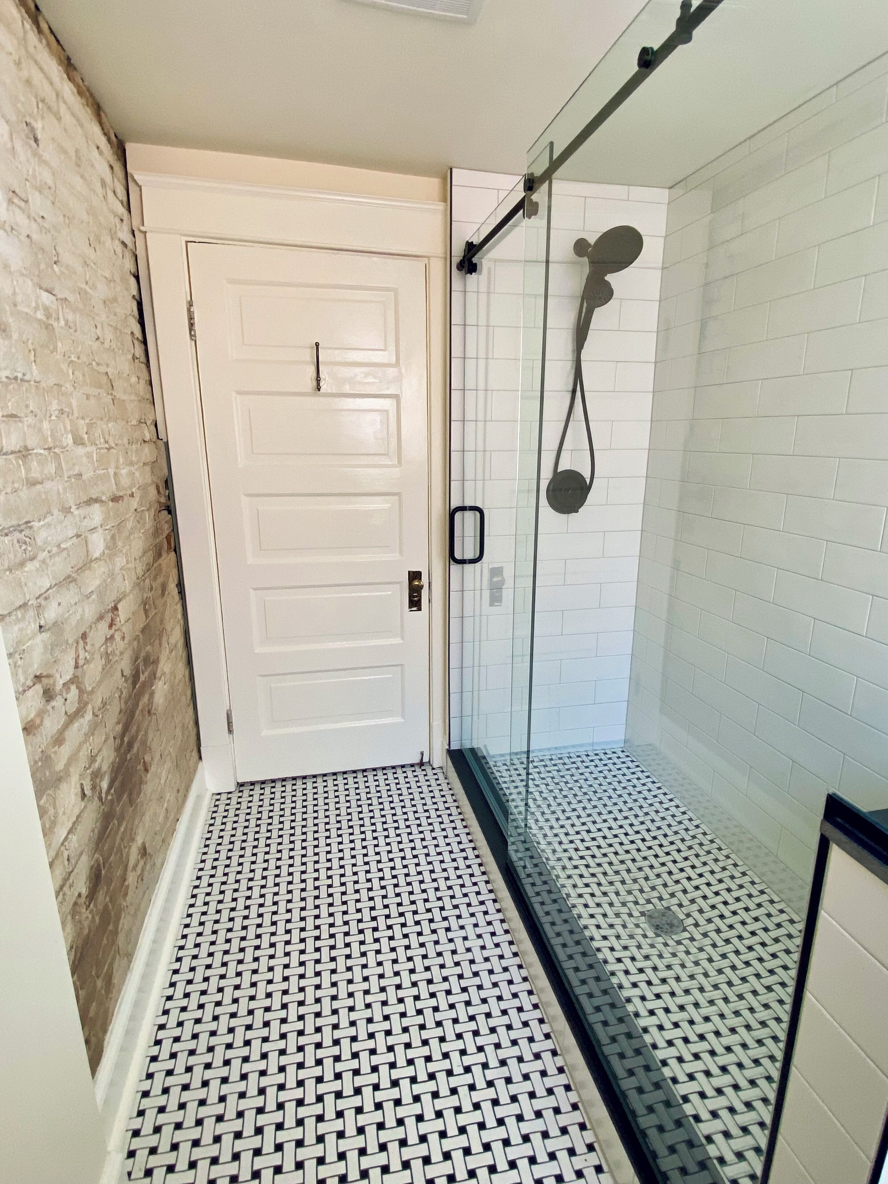 Une salle de bain avec une douche à parois de verre, une porte blanche et un carrelage décoratif.