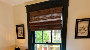 Un lit bien fait, agrémenté d’oreillers à motifs floraux, d’une courtepointe et d’une fenêtre donnant sur les bâtiments environnants.