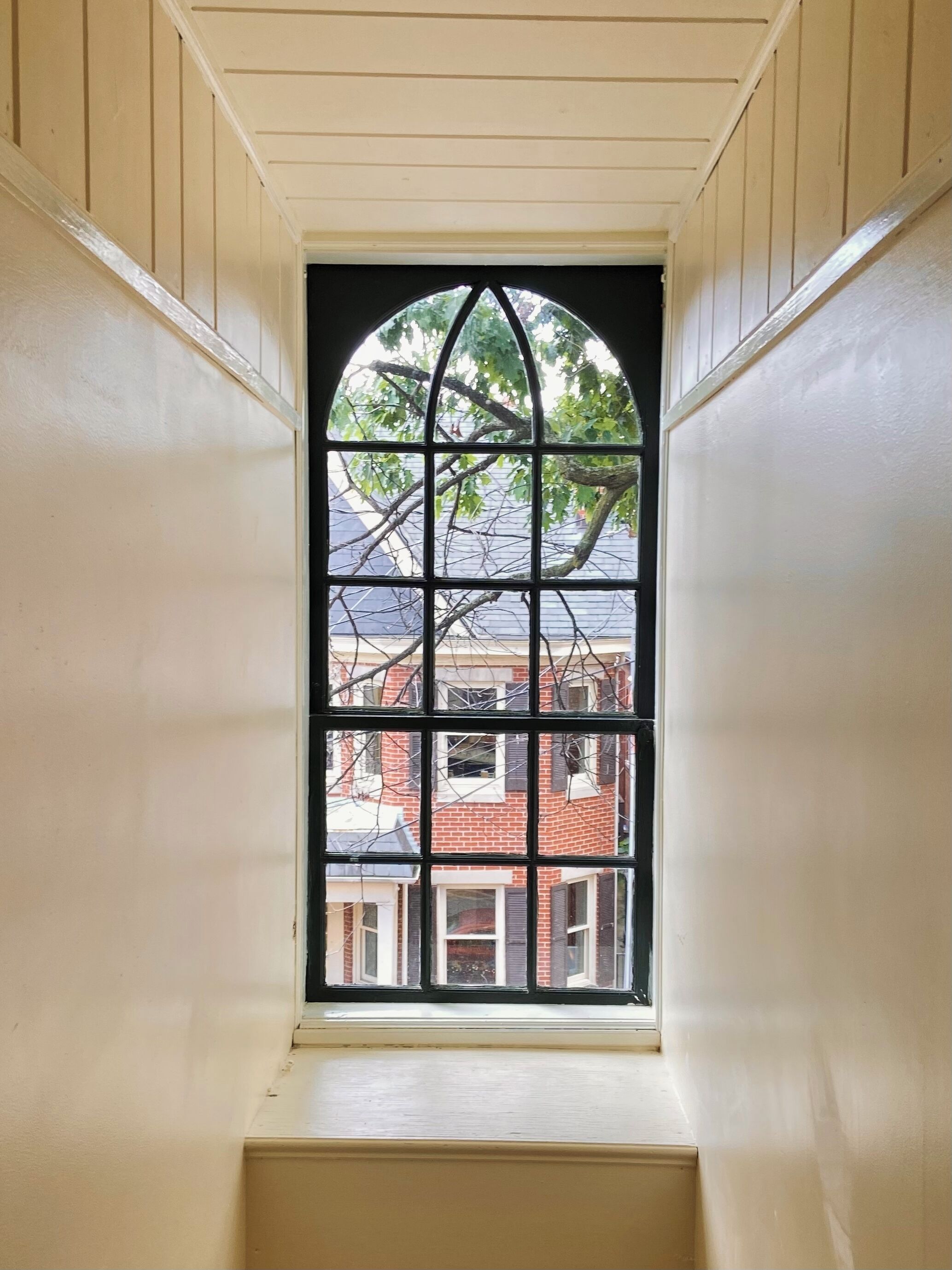 A narrow, white-paneled room with a window featuring a black frame and a grid pattern.