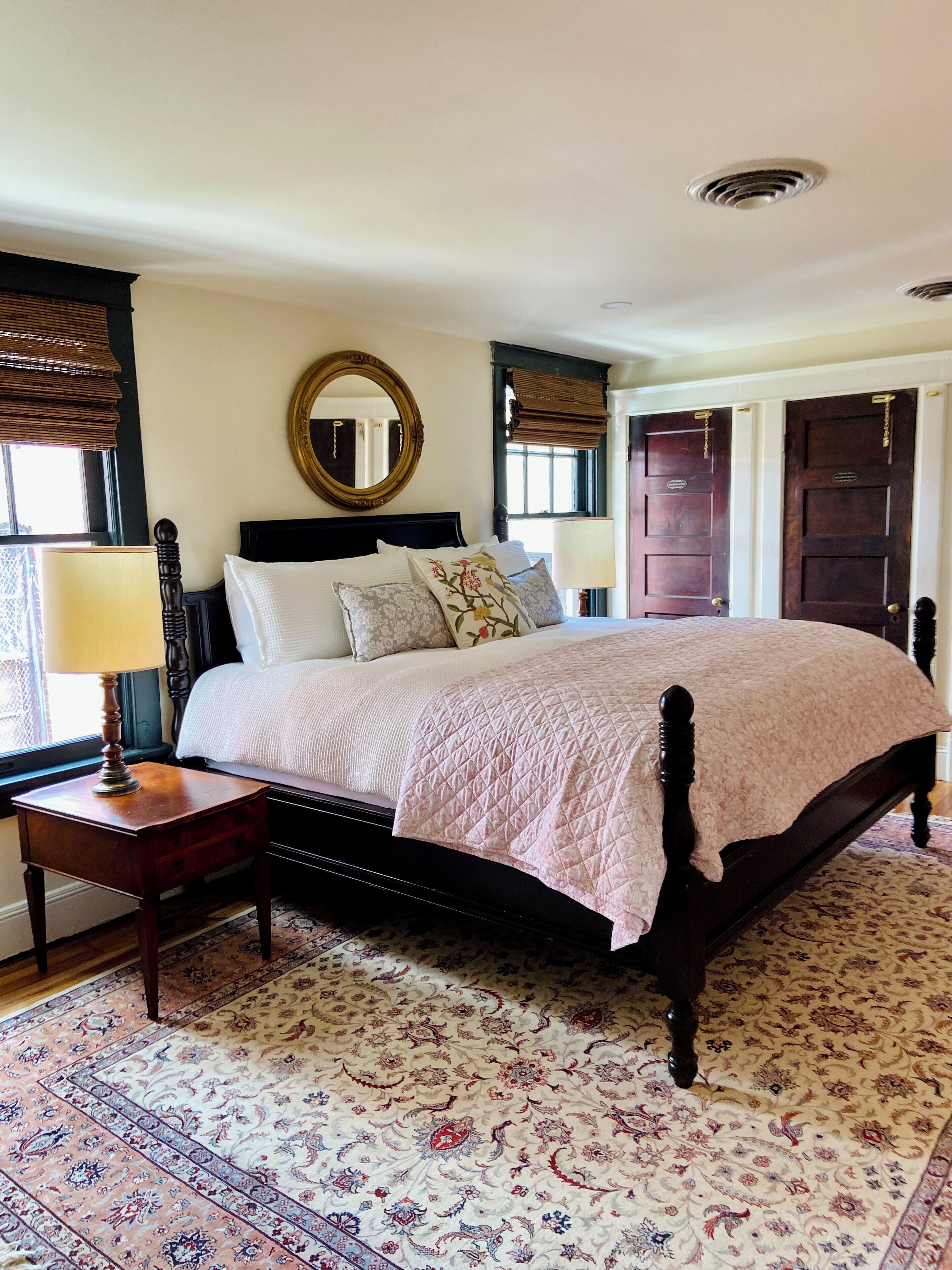 Een traditionele slaapkamer met een hemelbed, een ronde spiegel en een vloerkleed met dessin.