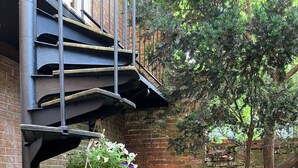 Une cour pavée de briques, agrémentée de différents pots de plantes, un sentier en pierre et un escalier en métal.