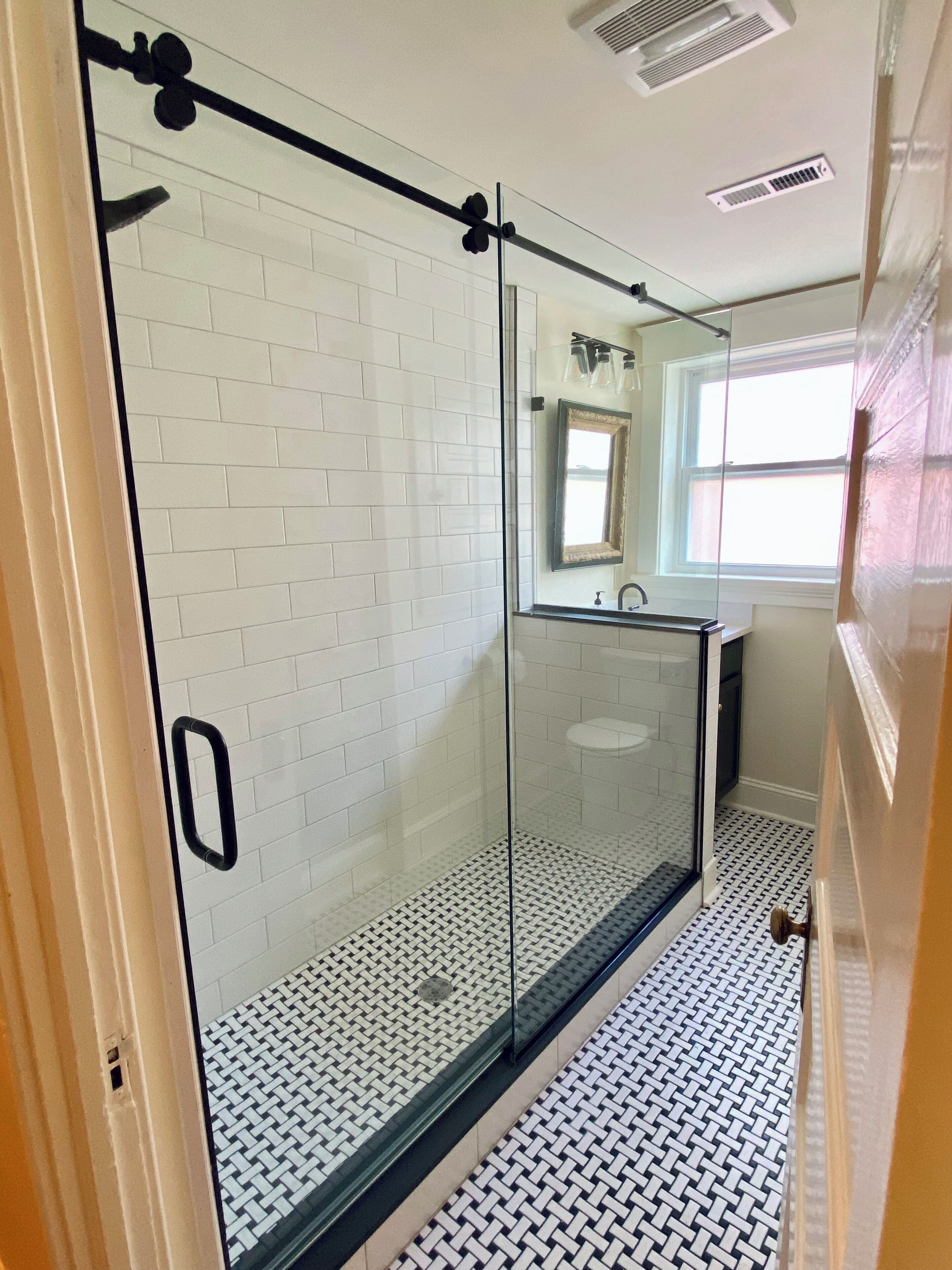 Een moderne badkamer met witte metro tegels, een douche met glazen wand en een vloer met een patroon.