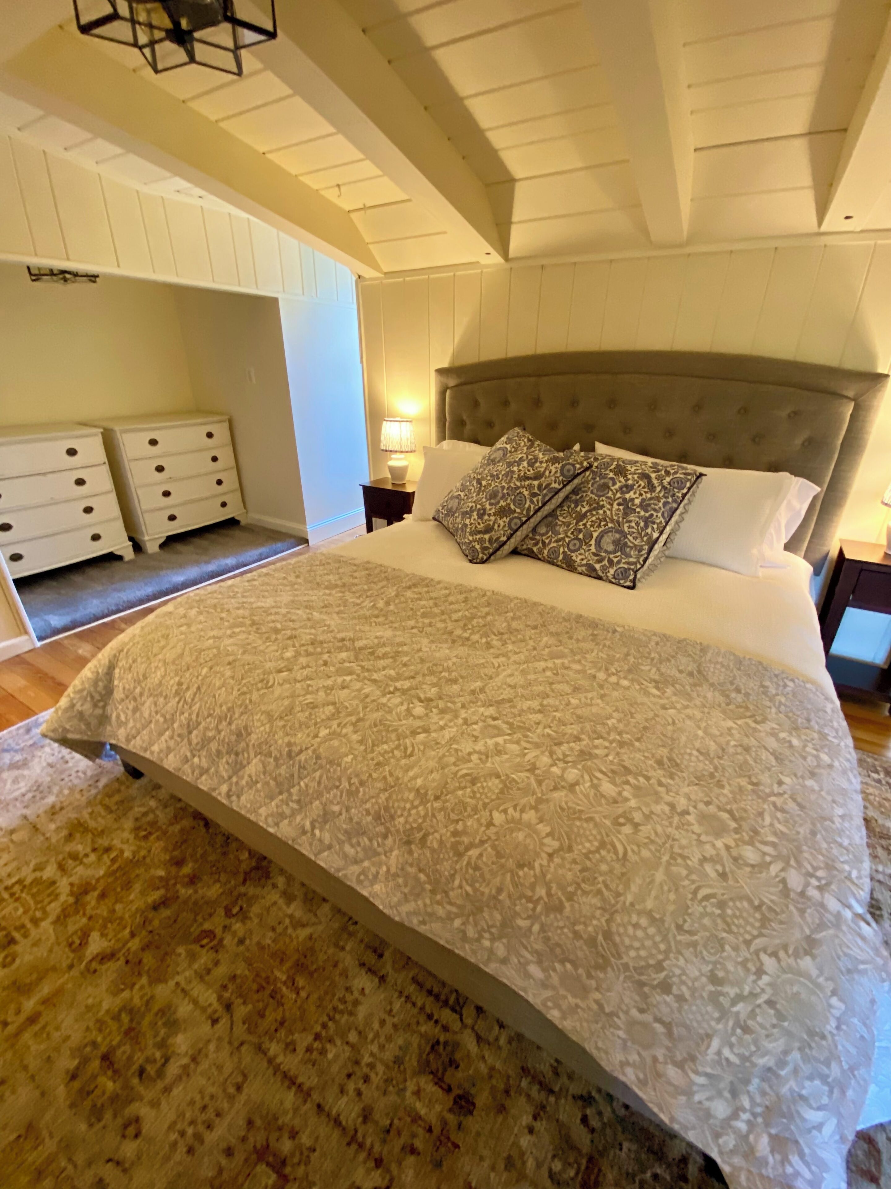 Une chambre à coucher avec un grand lit, deux tables de chevet, une lampe et un tapis à motifs.