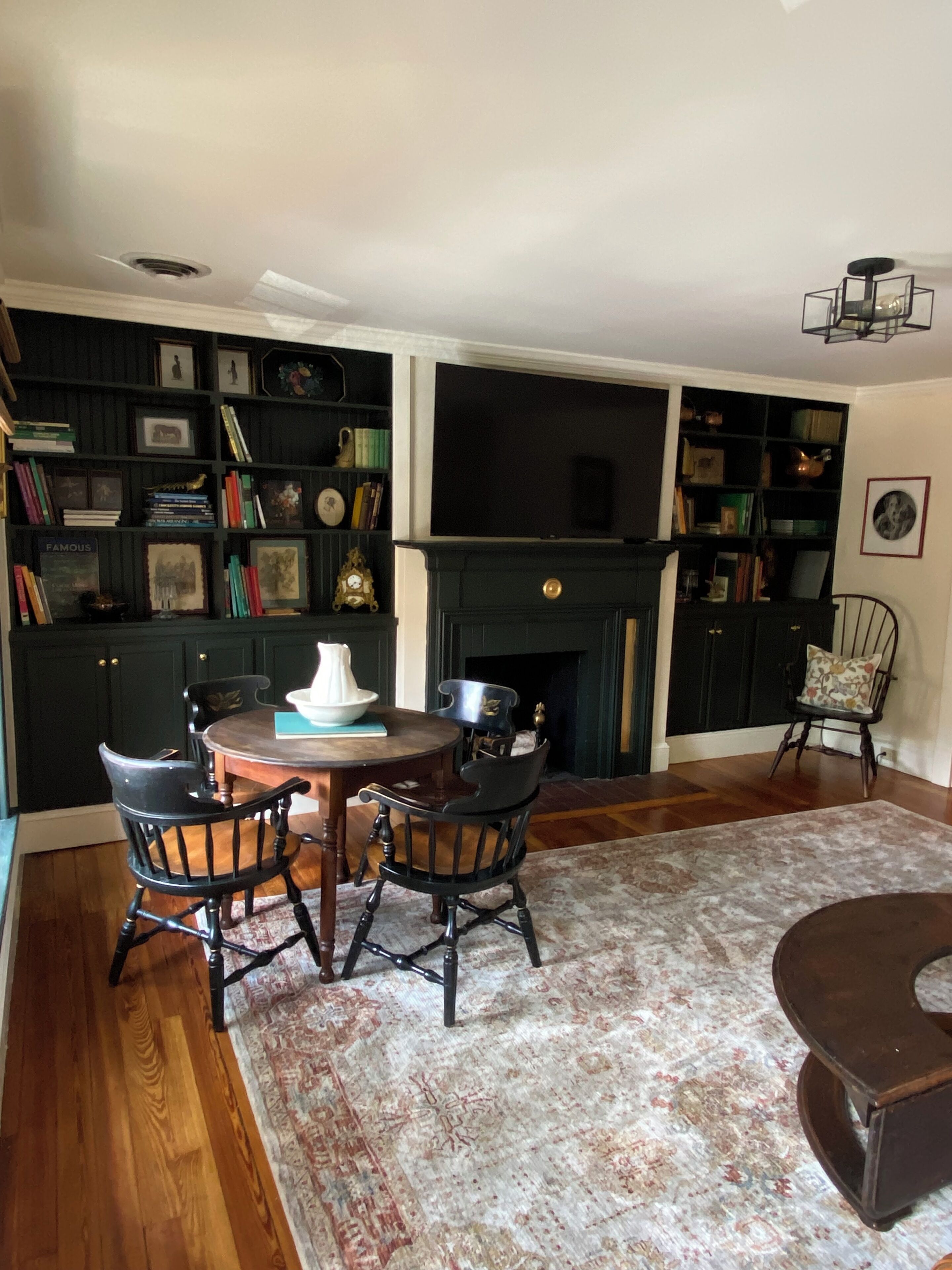 Una sala de estar con chimenea, un televisor montado encima y una estantería llena de libros y objetos decorativos.