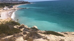 A coastal landscape with a beach, rocky terrain, and a distant building complex. - Calafell Beachfront Escape. Spacious Attic with Rooftop Terrace and Pool. (CT)