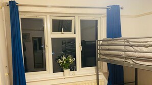 A room with a bunk bed, a window with blue curtains, a radiator, and a potted plant on the windowsill. - Cosy Double room - 2 guests -Close to central London-5minsHarrow and Wealdstone  (Harrow)