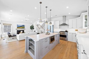 Una cocina amplia con una isla central, armarios blancos, electrodomésticos de acero inoxidable e iluminación colgante.